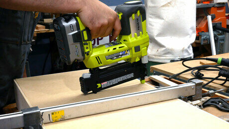 Cordless brad nail gun driving a nail into the bottom of a drawer