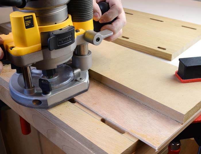 A yellow router sitting on a board routing mortises into the board.