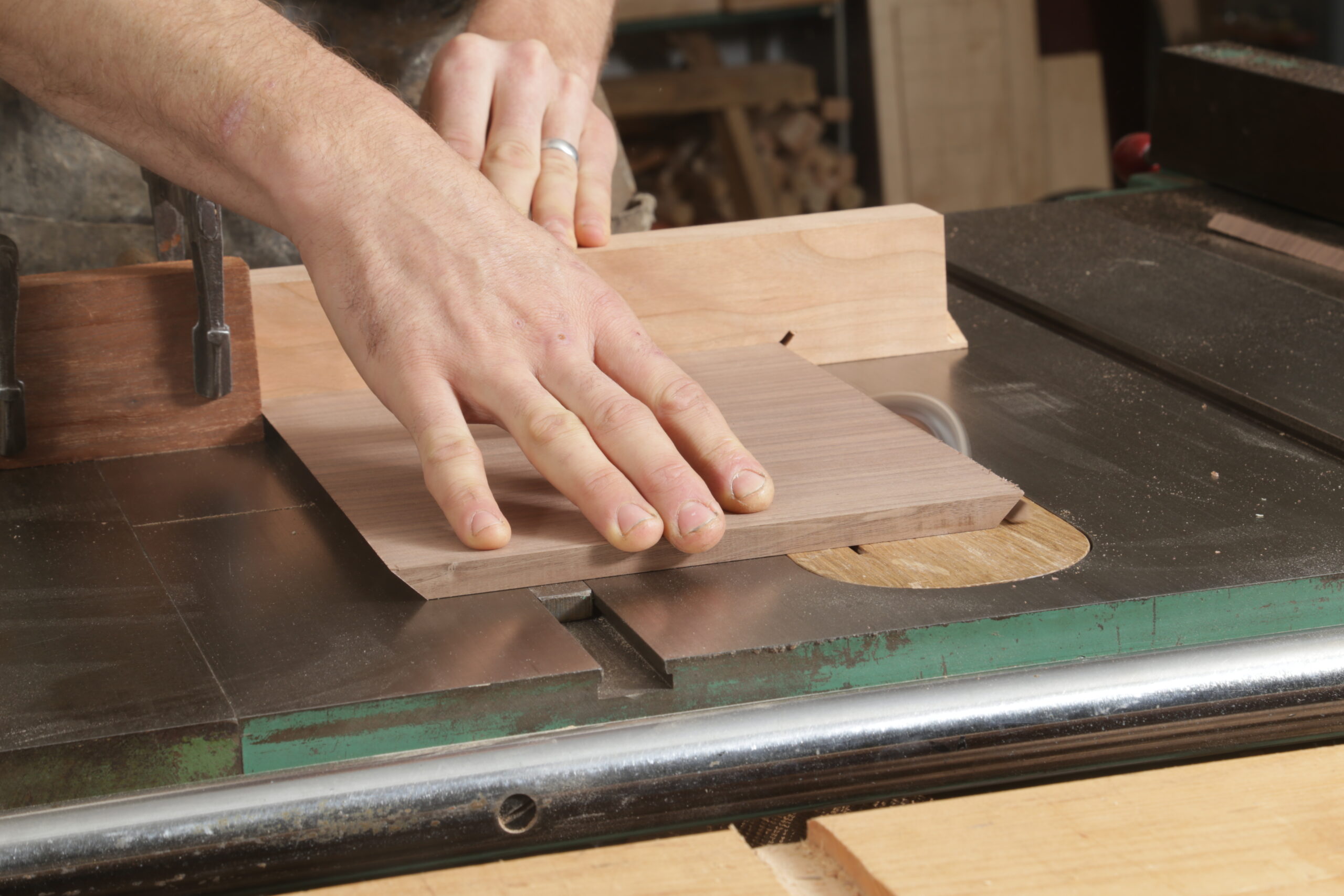 At the tablesaw, a tight shot of cutting thin a walnut board to 45° on one end. The other end has already been cut.