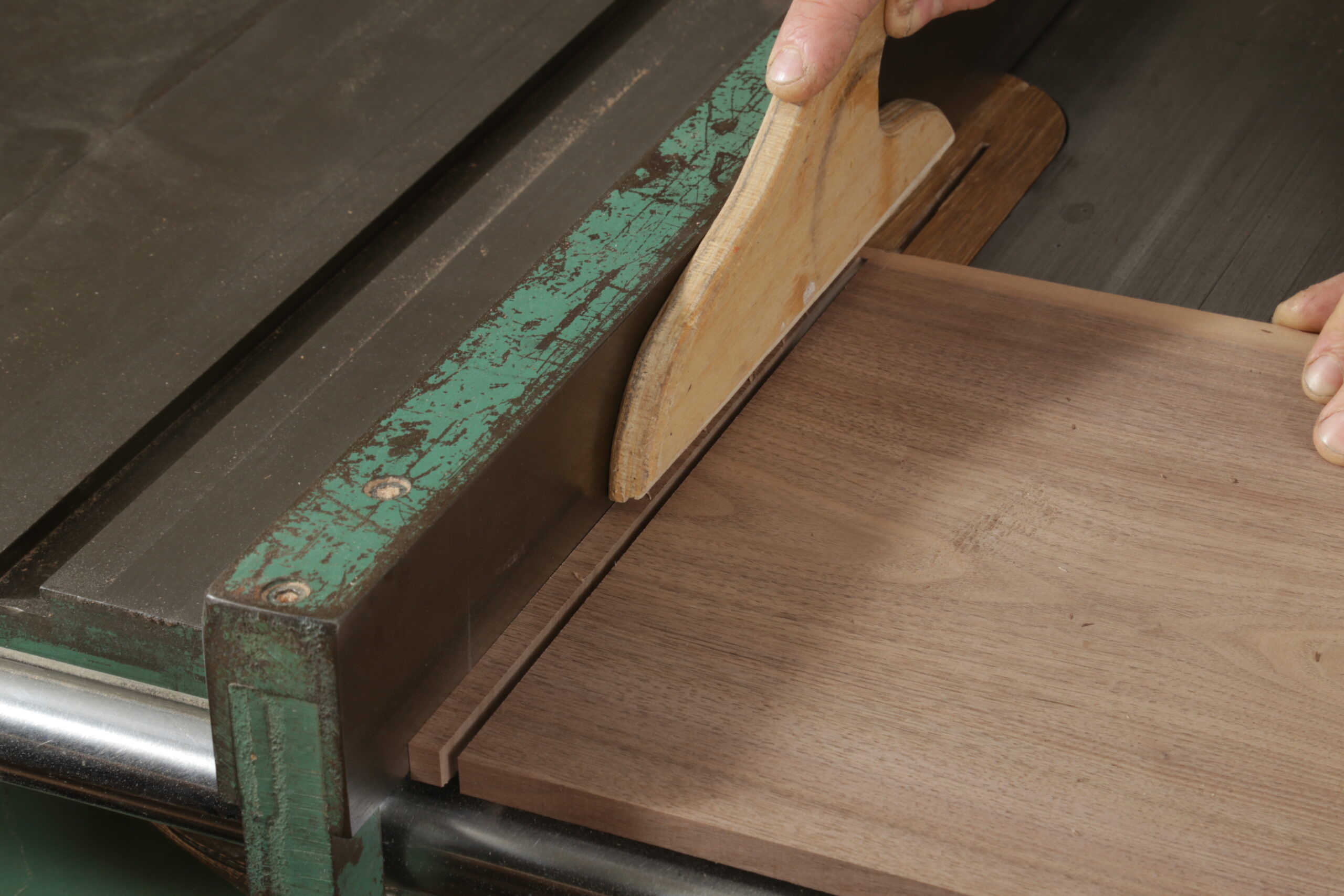 The author crosscutting a narrow strip from the end of a walnut board. This strip will be a runner for drawers. or safety, he is using a push stick to keep his right hand away from the blade.
