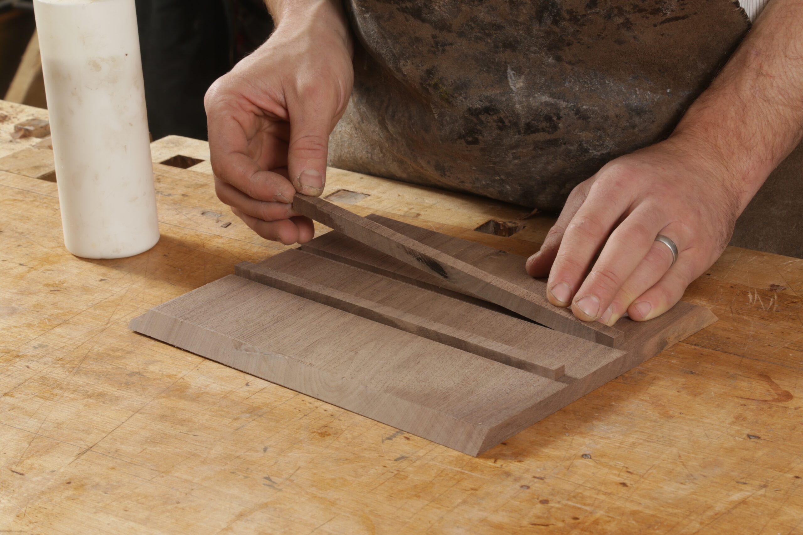 The author is gluing the second runner into the box side. The runners sit slightly proud of the inside surface of the box side, leaving a ledge for the drawers to ride on. There is a glue bottle in the background.