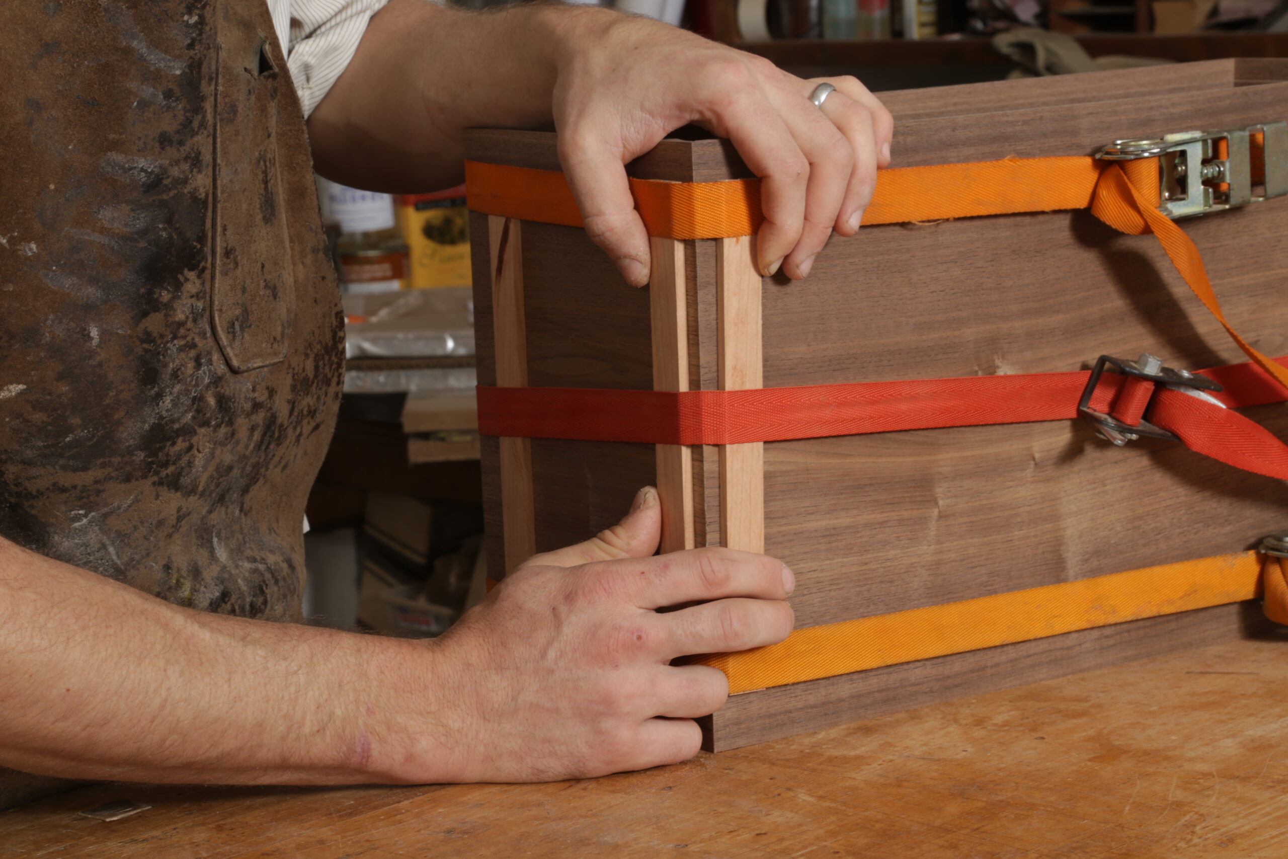 After tightening the ratchet straps, the author is pinching two strips of wood toward a corner of the box.